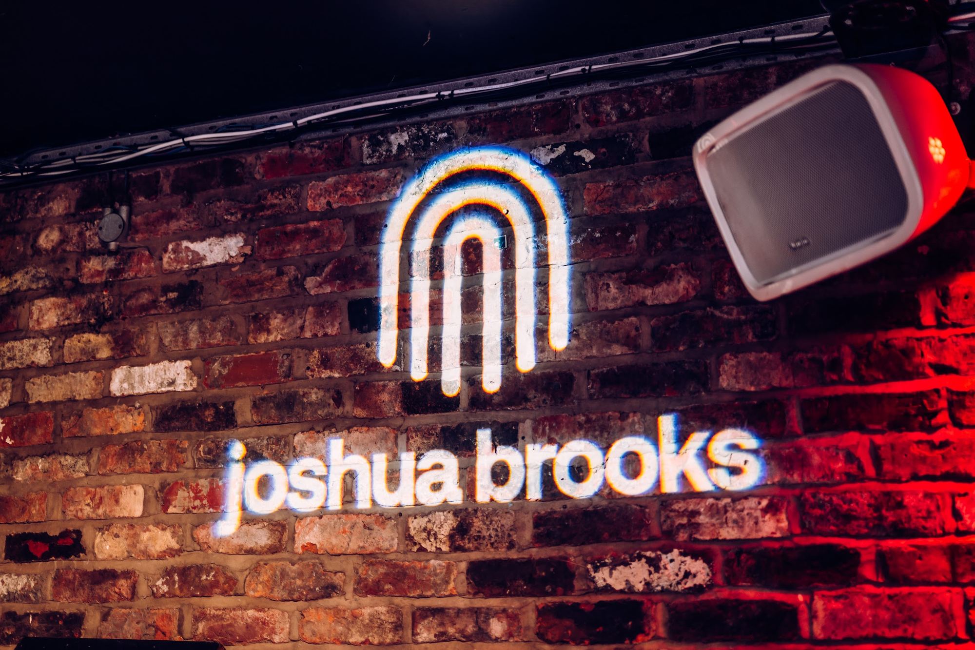 the joshua brooks arch logo projected on the basement brick wall